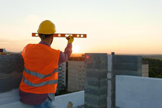 Construction worker using spirit level at building site with crane in background. photo