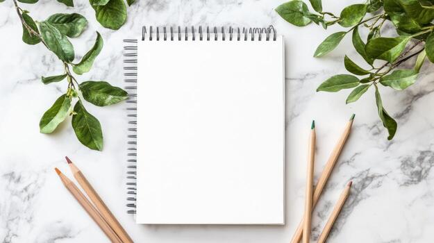 Blank spiral notebook surrounded by greenery on marble photo