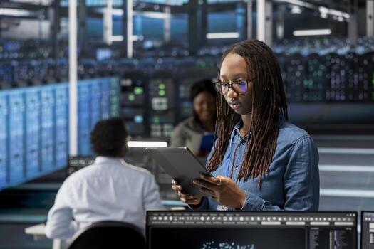 Data center admin using tablet to monitor system performance, identifying bottlenecks. Woman in server room using device to troubleshoot errors, implementing optimizations photo