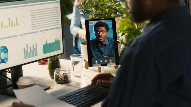 Worker in office talking with manager supervising tasks progression during online videocall. Employee discussing with supervisor overseeing work done during remote teleconference meeting, , camera A photo