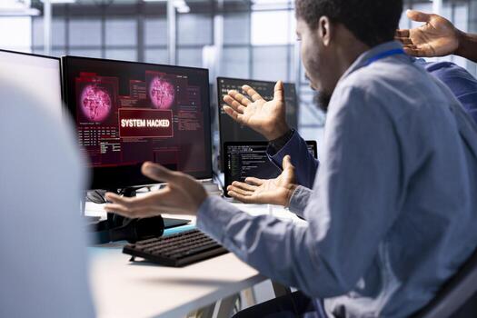 Team of african american engineers in server farm confused by hacker managing to pass firewall and stealing data. Critical error notification on monitor in data center bewildering colleagues photo