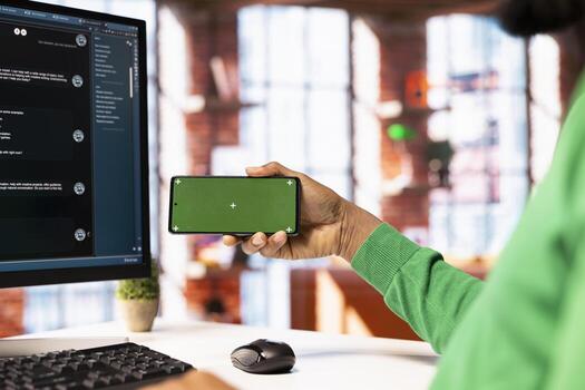 Man at desk watching on isolated screen phone about how to use AI LLM chatbot software. Person looking at tutorials on chroma key smartphone learning how to use large language model program photo