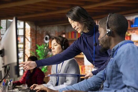 Asian call center manager providing guidance to multiethnic team, addressing questions. Customer support workplace onboarding specialist conducting orientation session for multiracial colleagues photo