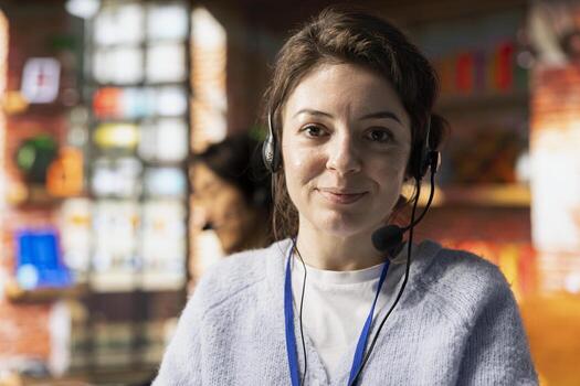Portrait of cheerful call center employee in office helping customers by answering questions, solving their issue. Joyous customer support worker using headset mic to talk with clients photo