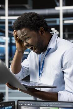 Upset server room technician screaming after making mistake and deleting all data backups. Livid man in data center raging after malfunction provoked by technical errors, unable to do system recovery photo