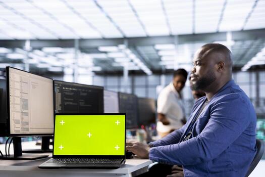 Technician in data center updates rigs systems on green screen laptop to protect servers from exploitable software vulnerabilities. IT professional using chroma key notebook to look for errors photo