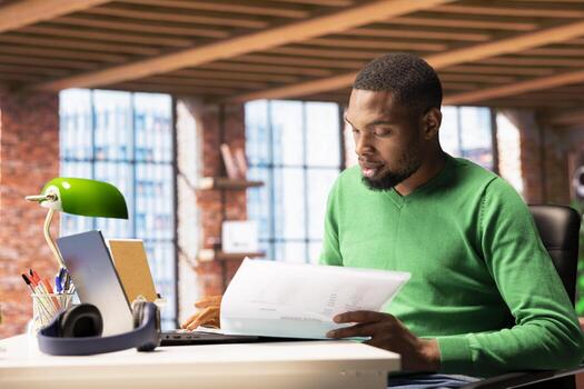 Man at home working accounting job, browsing though financial report pages. Remote worker reading paperwork containing economic graphs and figures, solving bookkeeping tasks photo