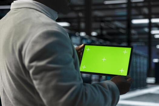 Close up of system administrator in data center using green screen tablet to check for server performance issues. IT specialist in server farm fixing errors slowing down hardware using mockup device photo