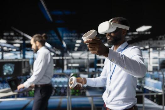 African american IT professional using VR technology to simulate AI neural network systems. Standing on industrial platform in data center using virtual reality headset with futuristic tools. photo