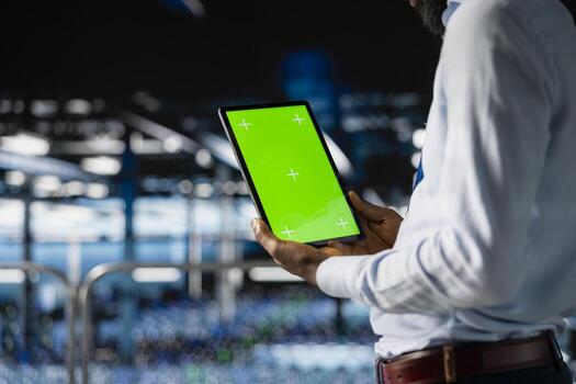 Male technician overseeing neural network using chroma key on tablet, reviewing LLM visualization. Server farm IT expert oversee rigs powering machine learning processes, industrial platform. photo