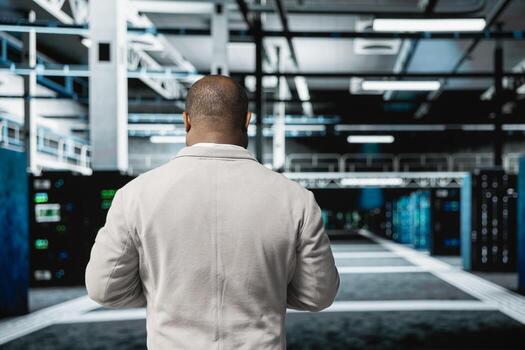 Engineer doing yearly checkup to prolong data center hardware life span and avoid downtime. African american employee in server room monitoring server infrastructure components photo