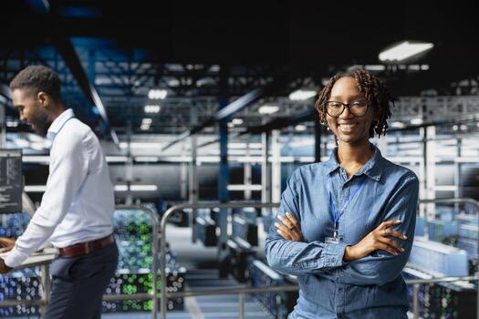 Happy IT expert in server hub reviews AI diagnostics on industrial platform, monitoring machine learning development. African american woman maintaining operational reliability, checkup. photo