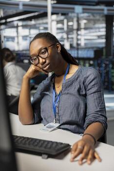 Exhausted server farm IT specialist strained after looking at computer screen for too long. Tired African american technician in data center stressed by long hardware troubleshooting session photo