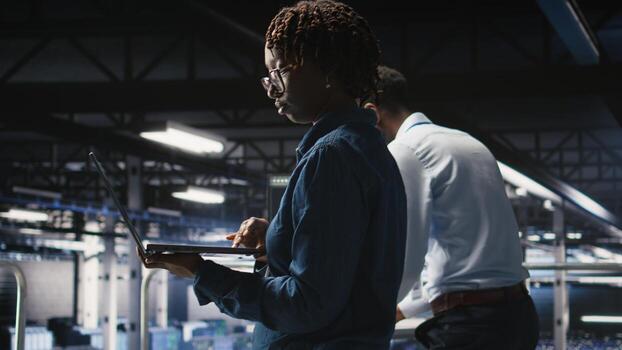 Data center engineer walking on industrial platform, running diagnostics on equipment to identify errors. Server farm IT professionals preventing rigs failure to minimize downtime, photo