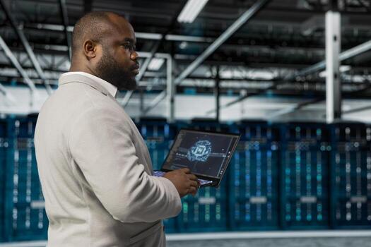 Data center system administrator using artificial intelligence computerized model on laptop. African american server room worker working with AI machine learning algorithms on device photo