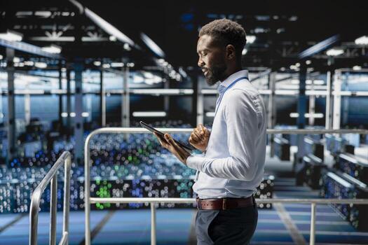 Young data center male employee on platform works on neural network software tasks. Confident african american engineer visualizing large language model architecture, technical support. photo