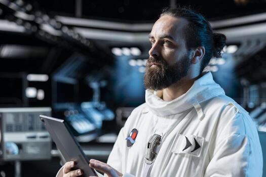 Scientist wearing cosmonaut gear in spaceship studying star charts on device. Astronaut researcher troubleshooting hardware using tablet while carrying out research aboard starship photo