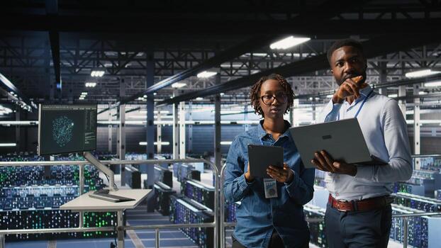 Data center admins running diagnostics on equipment using system monitoring tools to identify errors, doing brainstorming. IT experts work together to prevent failure and minimize downtime, photo