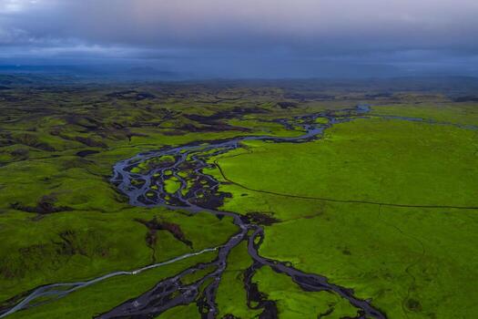Aerial view of Iceland's green terrain with dark rivers forming patterns, rolling hills in the distance, and an overcast sky adding contrast. photo