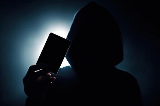 Mysterious figure in dark silhouette holding a device against a bright background photo