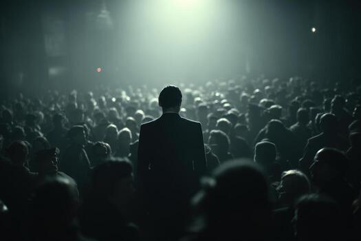 Man in a dark suit stands alone amidst a crowded gathering in dim light photo