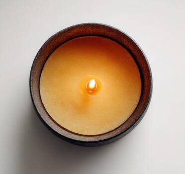 Overhead shot of a lit candle in a dark, textured container, sitting on a white surface photo