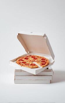 A small pepperoni pizza with a slice missing rests in a pizza box atop a stack of boxes photo