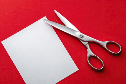 A pair of shiny scissors cutting white paper against a vibrant red background photo