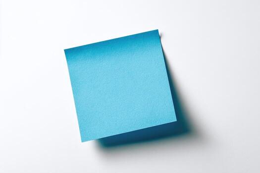 A square, pale blue sticky note is angled, lightly shadow cast on a bright white background photo