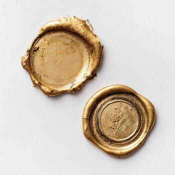 Two elegant gold wax seals, one with a design, on a white surface, top-down view photo