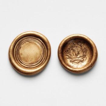 Two antique gold wax seals on a plain white surface, one plain, one with a raised design photo