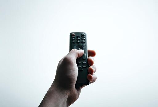 A hand grasps a dark remote control against a bright white background, pressing a button photo