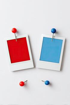 Two blank instant photos, one red and one blue, pinned on a white surface with pushpins photo