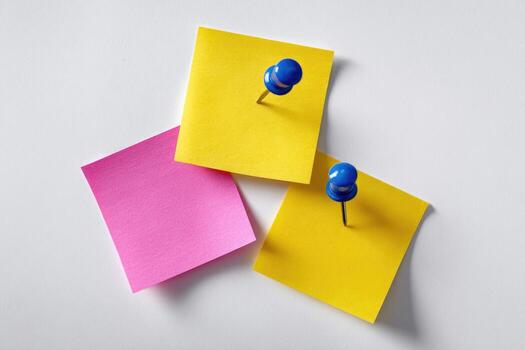 Three sticky notes pinned to a white surface, a pink and two yellow, with blue pushpins photo