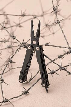 Close-up of a black multi-tool amidst tangled, grey barbed wire on a textured surface photo