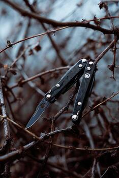 A closed butterfly knife rests on twig branches with a shallow depth of field in grayscale photo