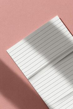Angled close-up of a lined paper pad against a textured pink surface, shadow photo