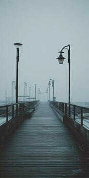 A misty pier extends into the distance, lined with lampposts, creating a moody and atmospheric scene photo