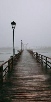 A wooden pier extends into a foggy atmosphere, featuring lampposts, railings, and a mysterious expanse photo