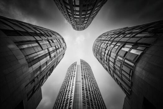 Low-angle shot of four towering skyscrapers converging towards a cloudy sky. Black and white photo