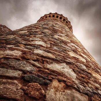 Low-angle shot of a stone-built, conical structure with a crenelated top against a cloudy sky photo
