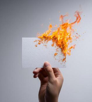 A hand holds a blank white card engulfed in a fiery explosion of orange flames photo