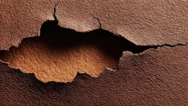 Textured brown leather with a large, jagged tear photo