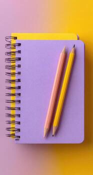 Two pencils rest on a lavender spiral-bound notebook. Bright yellow and light peach colored pencils. Pastel yellow and lavender background photo