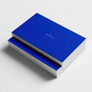 Two stacks of vibrant cobalt blue business cards, slightly overlapping, with a subtle iridescent texture and a small, white, sans-serif typeface logo photo