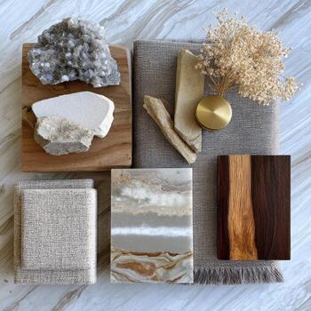 A curated collection of natural materials, showcasing various textures and tones. Beige, gray, and brown stones, woods, and fabrics are arranged on a light marble surface. A small, brass-toned object sits amidst the arrangement photo