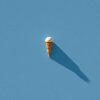 Overhead shot of single ice cream cone, casting a long shadow on a light blue backdrop photo