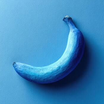 A blue-painted banana rests on a matching blue surface, casting a soft shadow photo