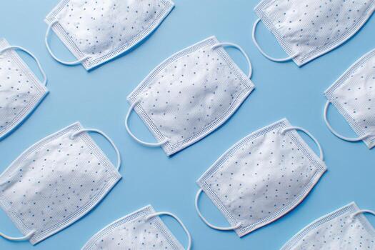 White face coverings with elastic straps on a light blue surface, arranged in a pattern photo