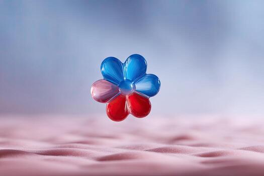 A colorful, glassy flower floats above a textured pink surface against a blurry blue backdrop photo
